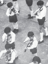 A black-and-white photo of many uniformed children standing and playing violin