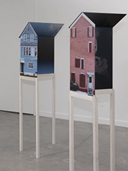 A photo of two sculptural works of houses on stilt legs in a gallery