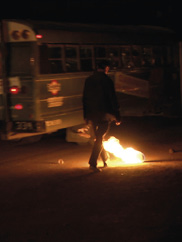 A video still of a person approaching an object on fire on the ground at night